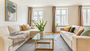 A modern living room with two sofas, a glass coffee table, a vase with flowers, and a framed abstract painting. - Regent 7 - Large 3 Bdr Apt with Balcony in City Centre (København)