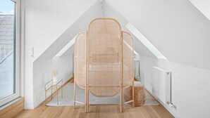 Un dormitorio tipo loft moderno con techo inclinado, una silla de ratán, una mesita y un radiador.