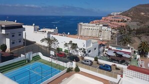 A residential area with a view of the ocean, a tennis court, and a building with multiple balconies. - Duplex • Walk to Anfi Beach • 3 Pools • Large Terrace (Los Caideros)