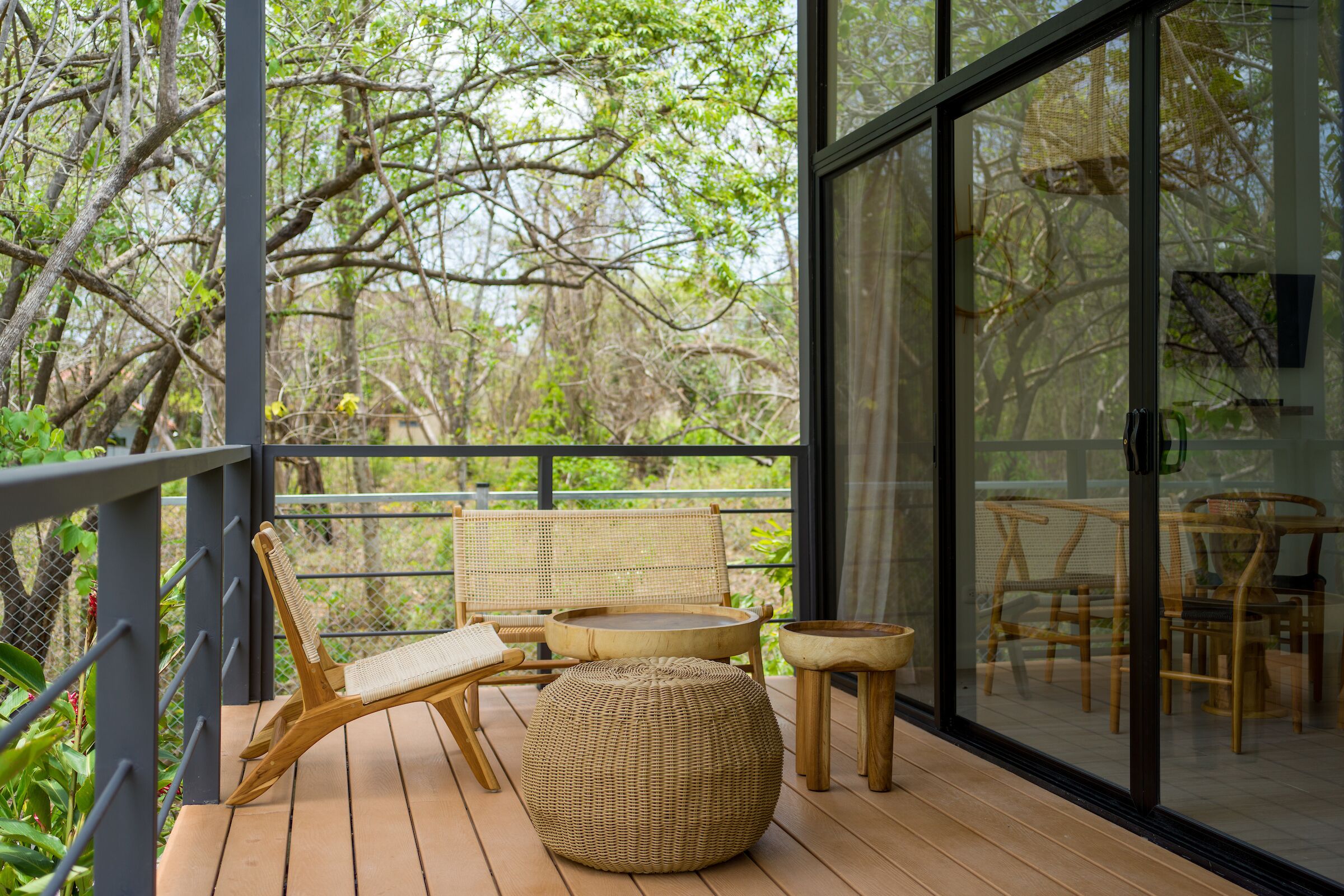 A wooden deck with wicker furniture, including a sofa, chairs, and a round table, overlooking a garden.