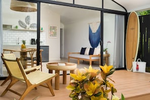 A modern living space with a glass door leading to a kitchen, a wooden dining table, and a surfboard. - 5 Favela Chic Adults Only 2 Bedroom Bungalow (Playa Langosta)