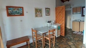 A dining area with a stone floor, wooden furniture, and a view into the kitchen. - Samos Island - Panorama Apartment with Jacuzzi (Koumeika)