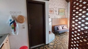 Une pièce avec un sol en pierre, un plafond en bois, une porte, un panier fixé au mur et un petit seau orange.