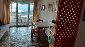 Ein Zimmer mit Steinboden, Holzbalkendecke, einem Esstisch mit Stühlen, einer Couch und Blick durch eine Glastür.