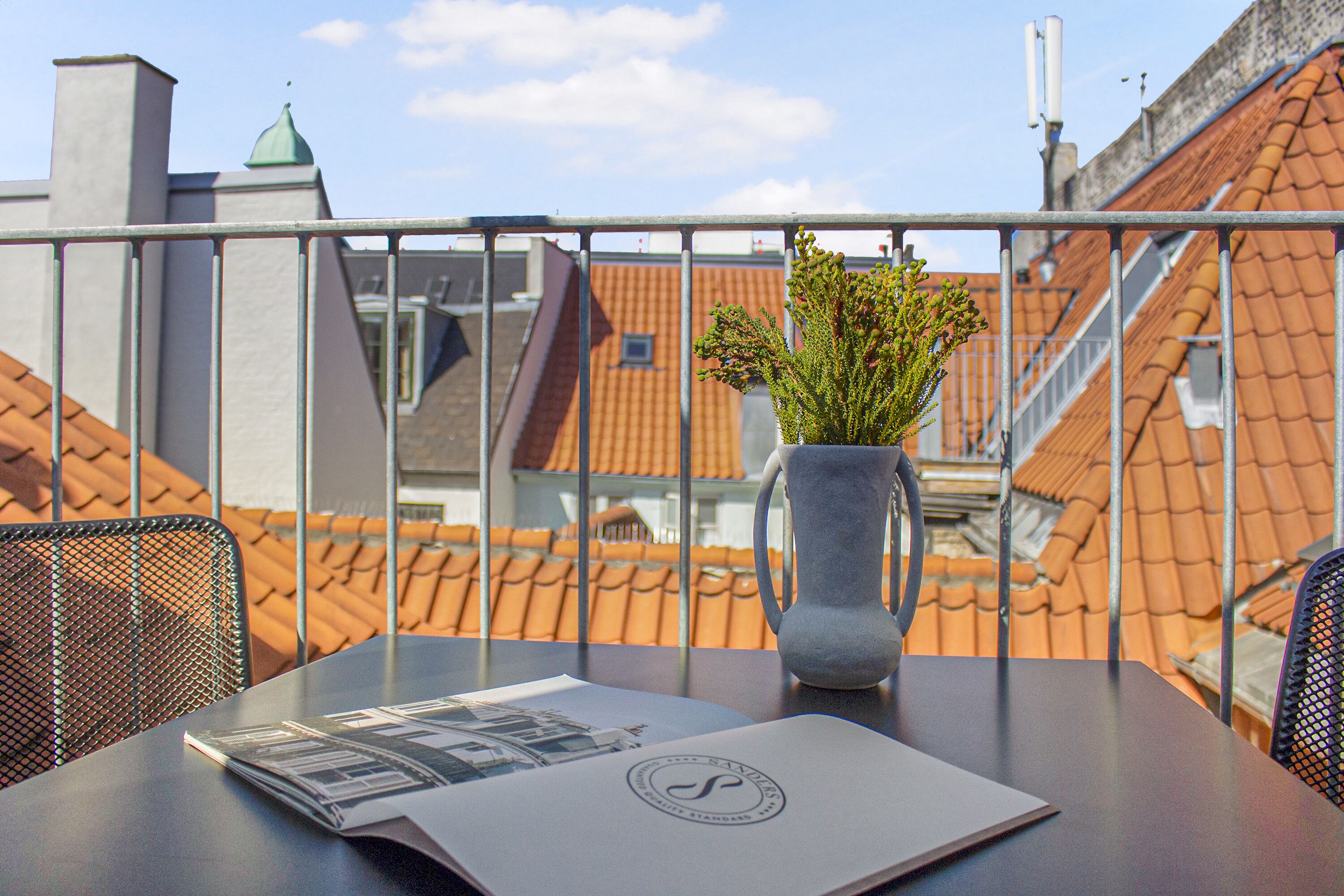 A balcony with a table, a vase with plants, and a magazine.