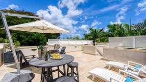 Une terrasse extérieure avec une table ronde, des chaises, un barbecue et un grand parasol.
