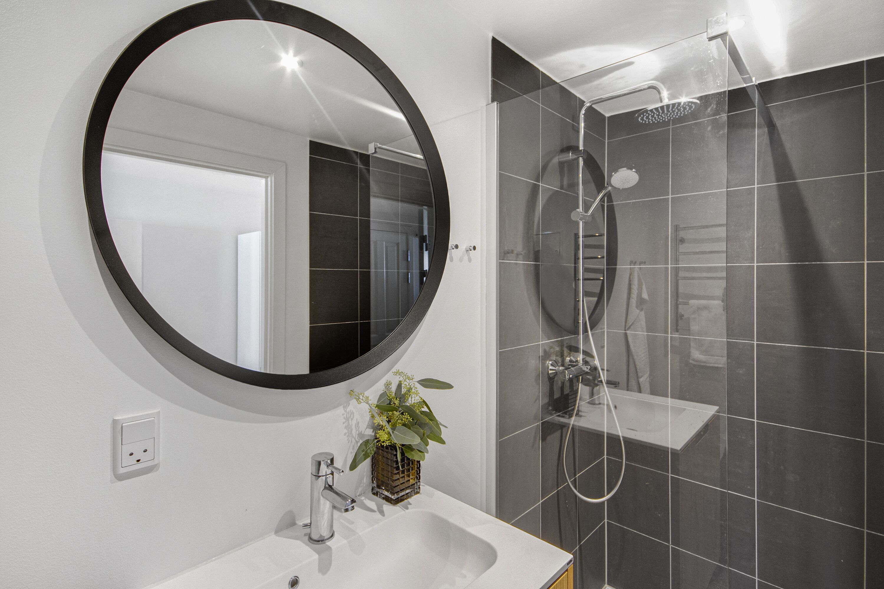 Une salle de bain moderne avec un miroir rond, un lavabo et une cabine de douche.