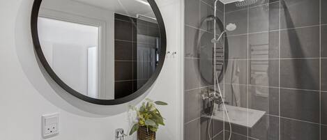 Une salle de bain moderne avec un miroir rond, un lavabo et une cabine de douche.