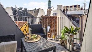 Eine Dachterrasse mit einem Korbsessel, einem kleinen Tisch mit Tablett und Topfpflanzen.