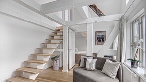 Ein modernes Interieur mit einer Holztreppe, einem grauen Sofa und einem Fenster mit Pflanze.