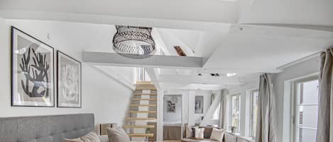 A spacious bedroom with a large bed, a staircase leading to an upper level, and large windows with curtains.