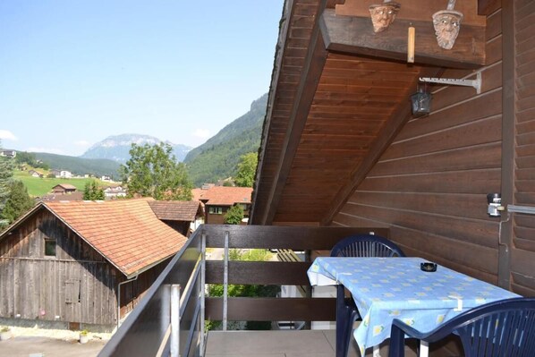 En træterrasse med et bord og stole, der giver udsigt over et bjerglandskab med huse.