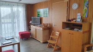 A room with a wooden desk, a television, a red chair, and a bookshelf.