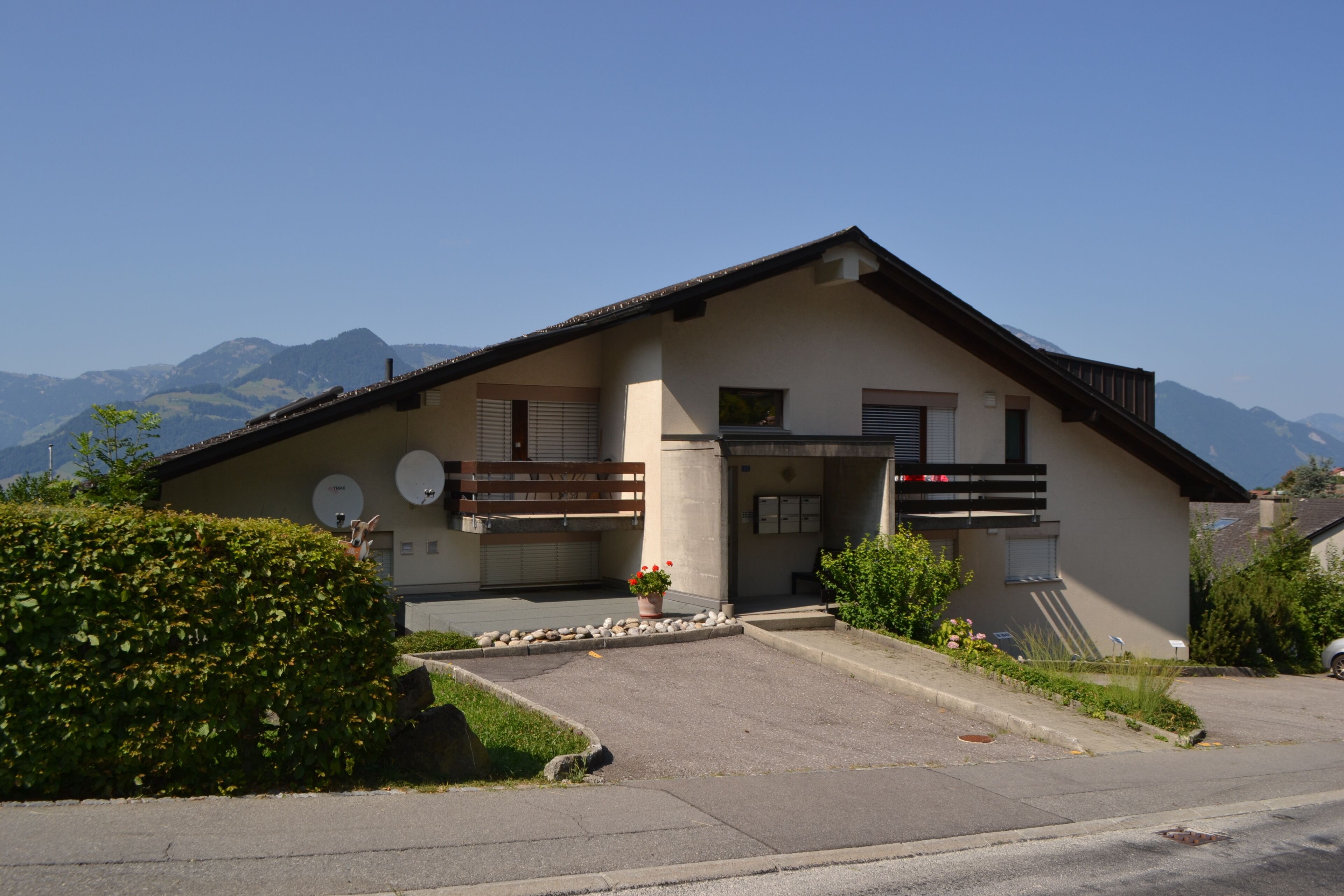 A two-story house with a sloped roof, satellite dishes, and a small garden with a potted plant.