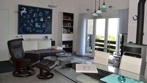 A modern living room with a glass coffee table, a black leather chair, a sofa, a bookshelf, and a large wall art piece. - Two-bedroom Apartment for 4-5 guests with lake and mountain views (Emmetten)