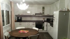 Et kompakt køkken med hvide skabe, et spisebord med stole, en mikrobølgeovn og et køleskab.