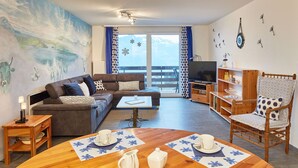 Ett modernt vardagsrum med en soffa, ett matbord med en blommig bordslöpare, en tv och en balkong med utsikt.