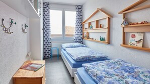 Ett sovrum med två sängar, ett skrivbord i trä och ett fönster med gardiner.