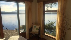 Una habitación con una cama, una silla y amplios ventanales con vistas al agua.
