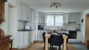 Une cuisine moderne avec des meubles blancs, une table à manger pour quatre personnes et une machine à café.