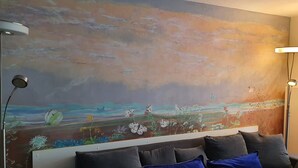 Un salon moderne avec un grand tableau abstrait au mur, un canapé de couleur foncée agrémenté de coussins bleus et deux lampadaires.