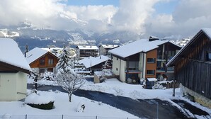 A snow-covered village with buildings, a road, and mountains in the background.