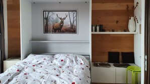 A bedroom with a bed, a mounted picture of a deer, a bookshelf, and a small table.