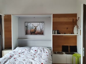 Une chambre à coucher avec un lit, un tableau représentant un cerf accroché au mur, une étagère remplie de livres et un vase contenant des plantes séchées.