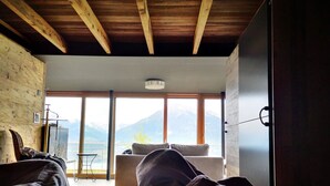 Une chambre à coucher avec un lit, une chaise et une vue sur les montagnes, visible à travers de grandes fenêtres.