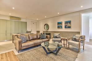 A modern living room with a leather sofa, a glass coffee table, a patterned rug, and a fireplace.