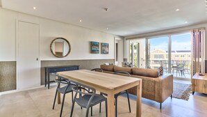 Ein modernes Wohnzimmer mit einem Holzesstisch, grauen Stühlen, einem braunen Sofa und einem großen Fenster mit Blick ins Freie.
