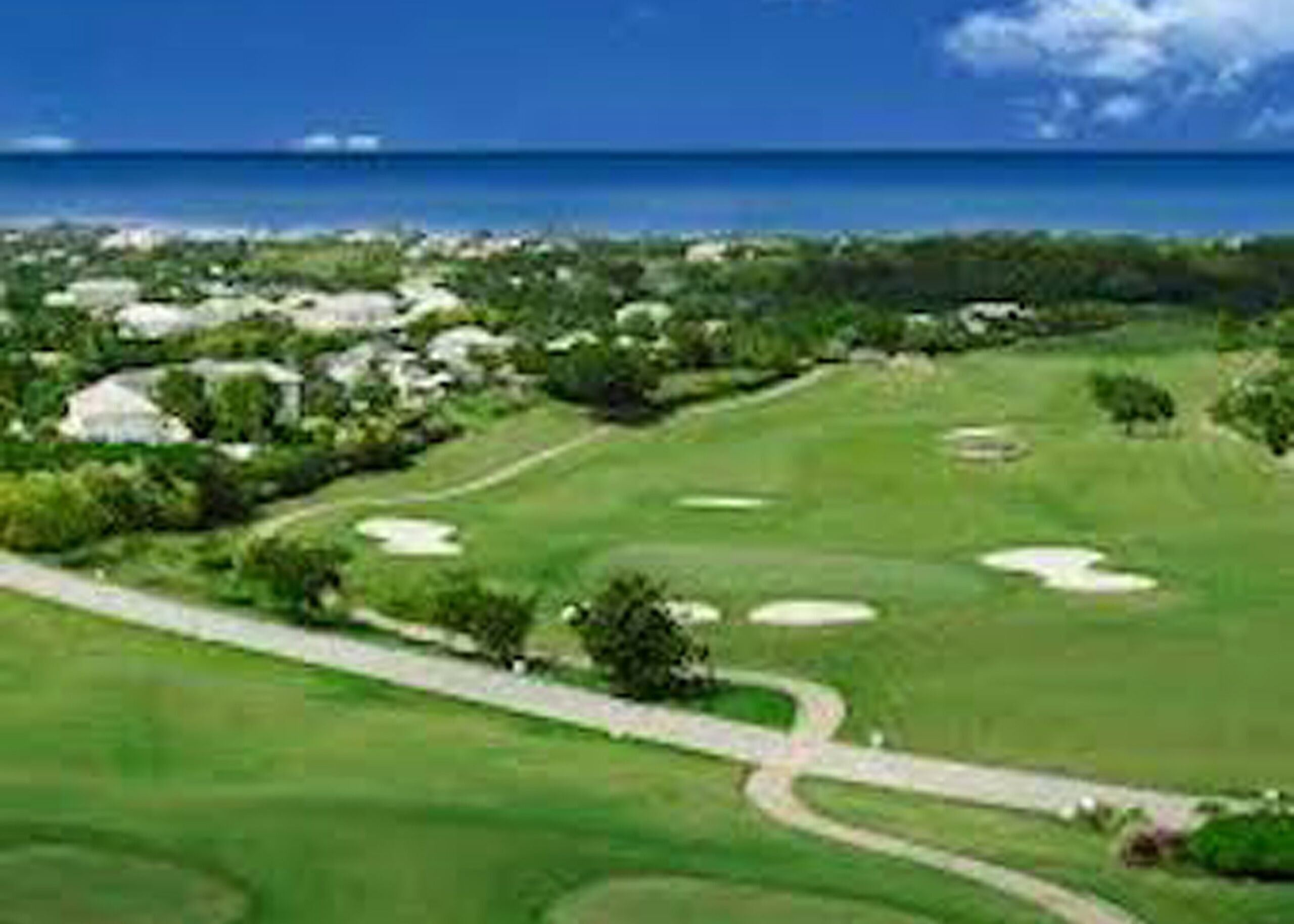 A golf course with a view of the ocean and residential buildings in the background.