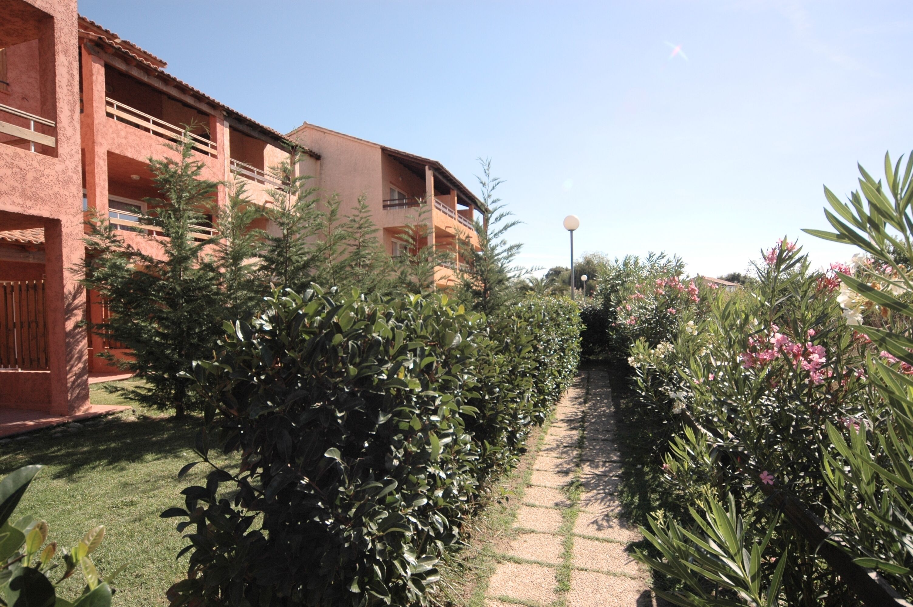 Un chemin de jardin menant à un bâtiment doté de nombreux balcons, avec un ciel dégagé.