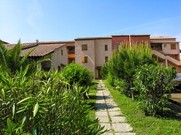 A pathway leading to a building with multiple balconies and a tiled roof.