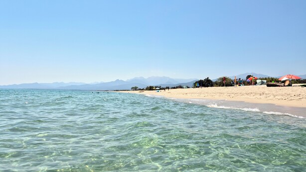 A beach with clear water, a sandy shore, and distant mountains.