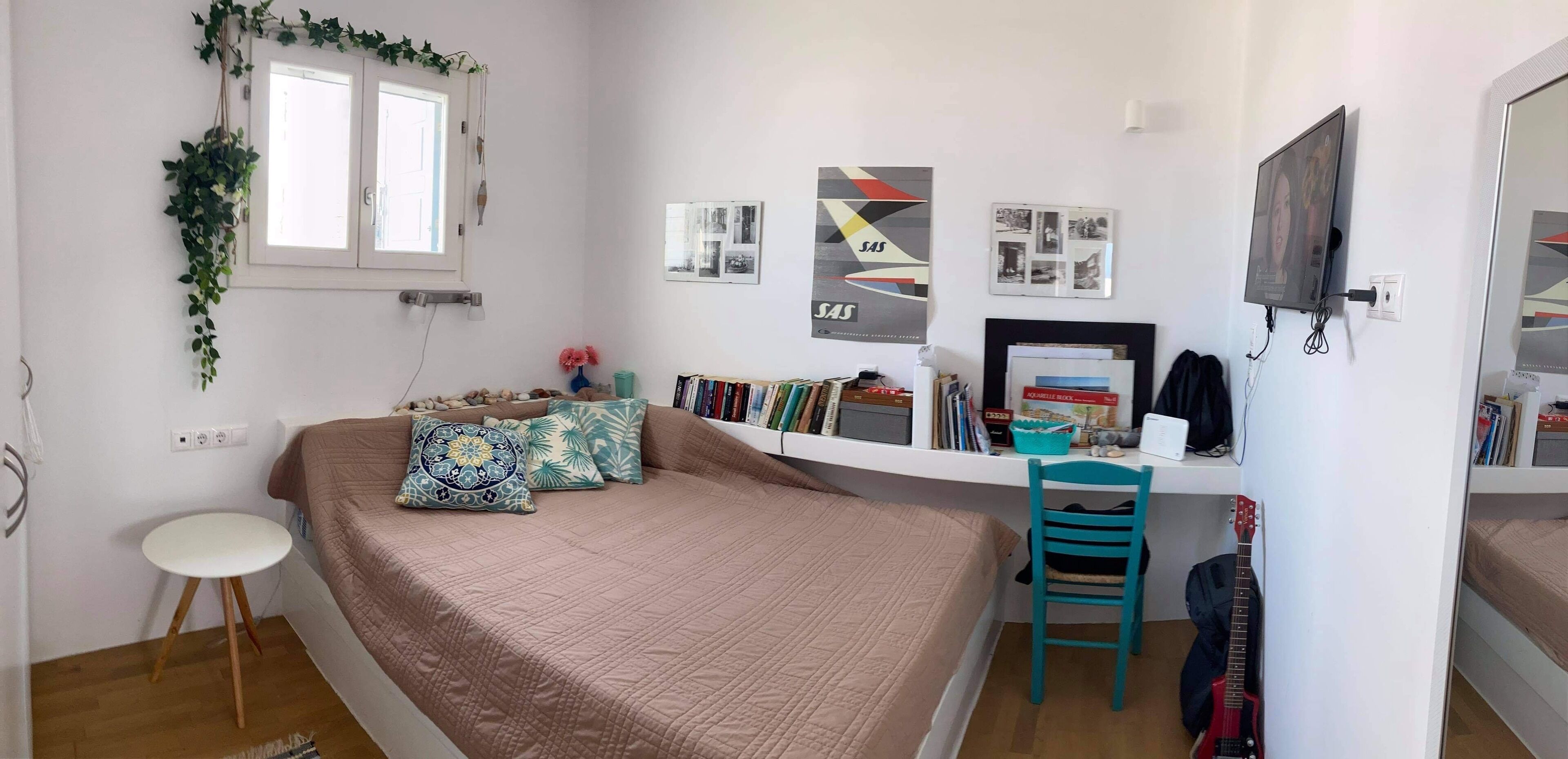 A bedroom with a bed, a desk, a chair, a guitar, and a bookshelf.