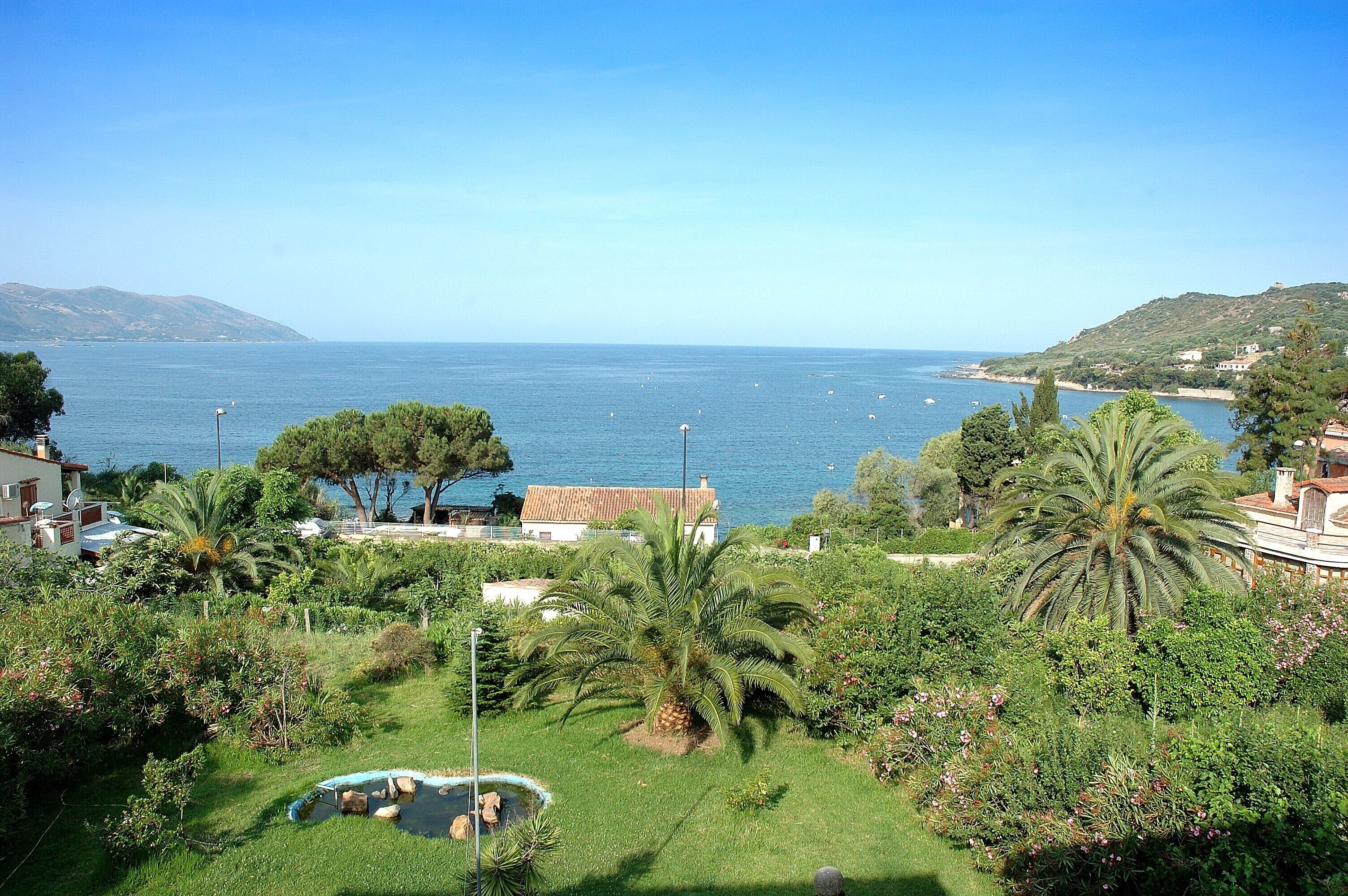 A coastal property with a pool, lush greenery, and a view of the sea.