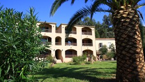 A multi-story building with balconies, surrounded by greenery and a palm tree.