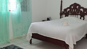 Ein Schlafzimmer mit einem hölzernen Bett, einem kleinen Nachttisch, einer weißen Bettdecke, einem grünen Vorhang und einem grauen Teppich.
