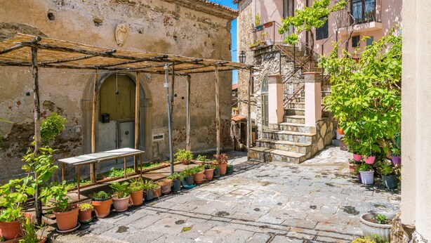 A narrow cobblestone street with a rustic building on one side and a staircase leading to a balcony on the other. There are potted plants and a wooden table under a pergola. - Ecolodge Selvitelle - Escape the hectic and submerge in the nature of Cilento (Cicerale)