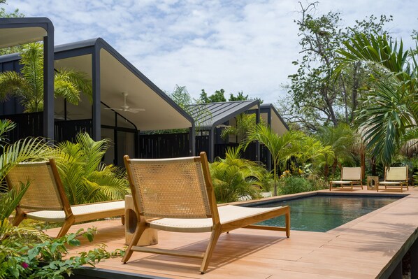 Zona junto a la piscina con sillones de descanso, una pileta y abundante vegetación.