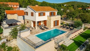 Eine zweistöckige Villa mit Swimmingpool, Steinmauern und Blick auf die umliegenden Hügel.