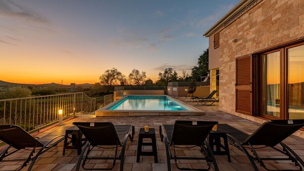 Ein Pool auf dem Dach mit Liegestühlen, einem Tisch und Blick auf den Sonnenuntergang.