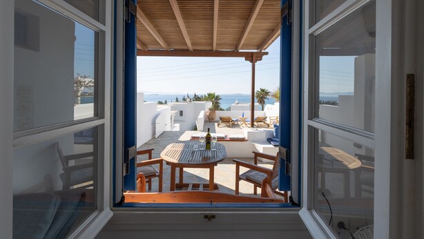 A balcony with a wooden table and chairs, a view of the sea, and white buildings in the background. - Beach House with Seaview (Naxos)