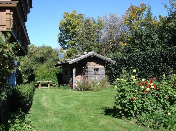 A rustic wooden cabin with a sloped roof, surrounded by a well-maintained garden with various plants and flowers.