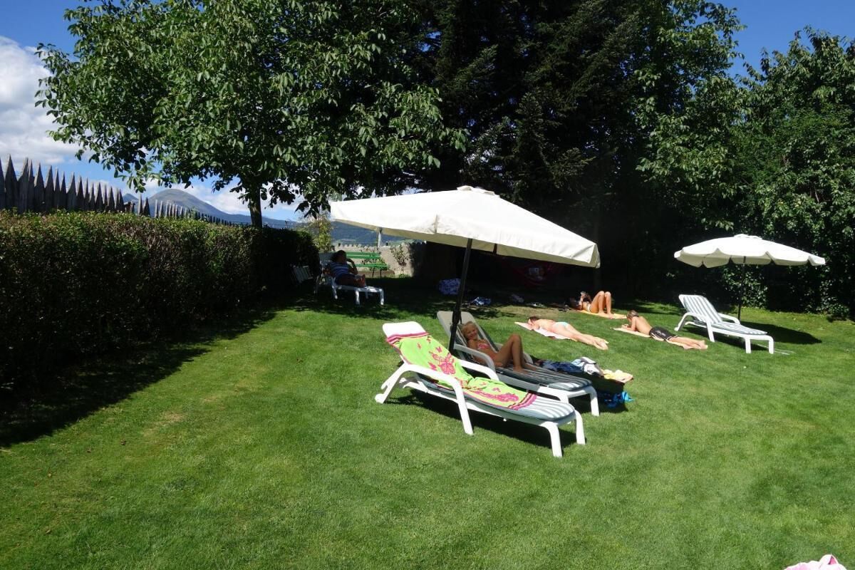 A grassy outdoor area with lounge chairs and umbrellas, a hedge, and a distant mountain view.