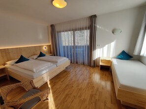 Ein Zimmer mit zwei Betten, Holzboden, einem Fenster mit Vorhängen und einem Nachttisch.