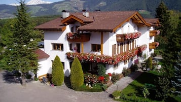 Un bâtiment blanc avec un toit brun, entouré de verdure et de montagnes.