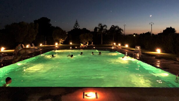 Una piscina iluminada de noche, rodeada de árboles y un cielo despejado.
