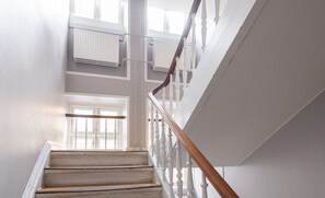 Un escalier avec des balustrades blanches et une main courante en bois menant à un palier doté d’une porte et de fenêtres.